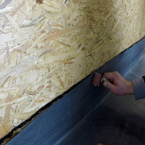 Verstreichen des schwarzen Anschlussklebers Flex mit einer Rolle auf einer Dachfolie