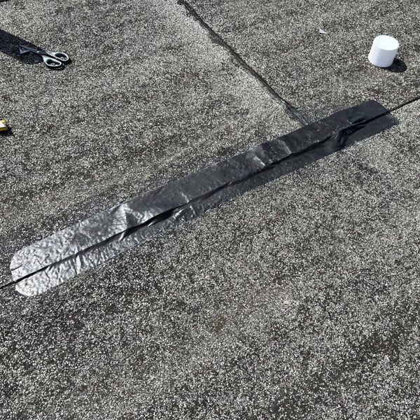 Schwarzes Dach Reparaturband auf dunklem Dach, Schere und weisse Rolle im Hintergrund