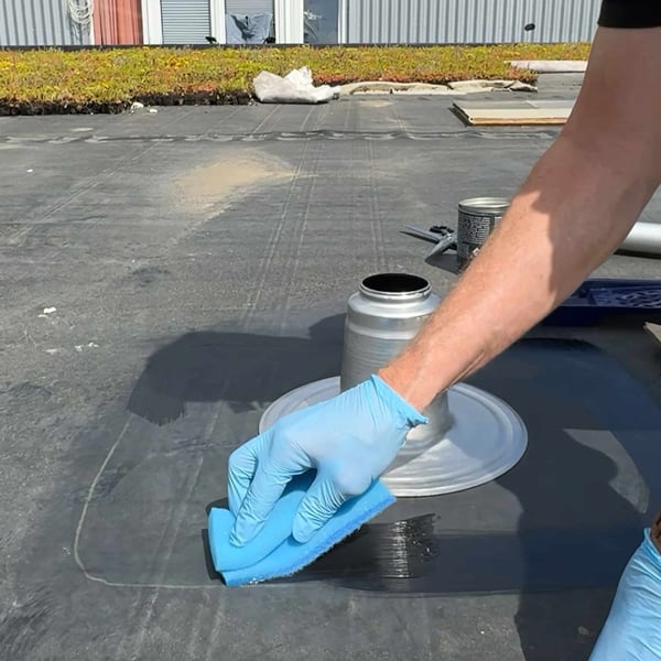EPDM Aktivierung wird mit blauem Schwamm um ein Dachablaufrohr aufgetragen