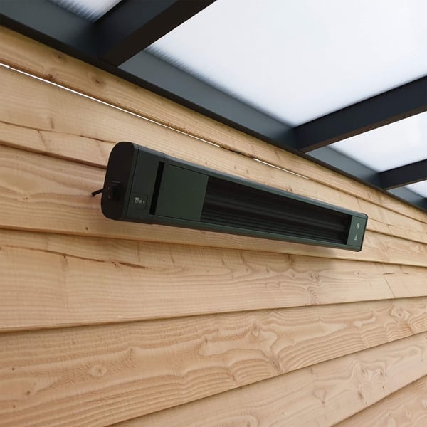 Schwarze Aluminium-Heizung an Holzwand, leicht schräg von vorne, unter transparentem Dach
