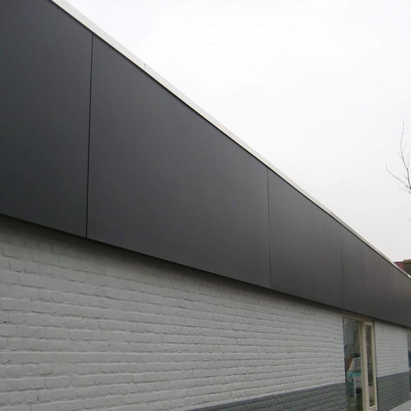 Dunkelgraue HPL Platten als Dachrandverkleidung ueber einer weissen Ziegelwand