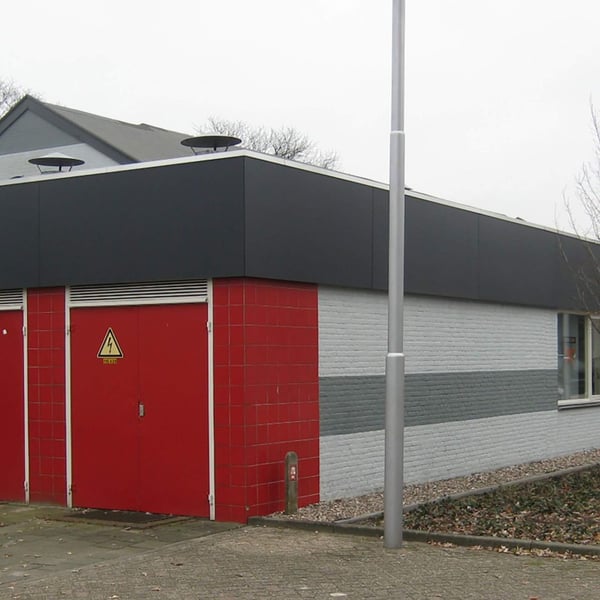 Gebäude mit dunkler Plattenverkleidung oben, rotem und grauem Mauerwerk unten, rote Türen