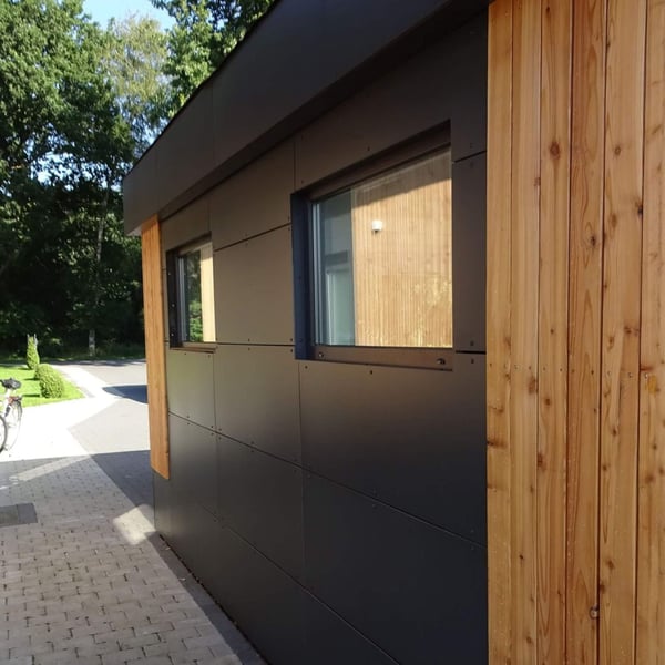 Seitenansicht eines Gebäudes mit dunklen HPL Platten und Holzverkleidung