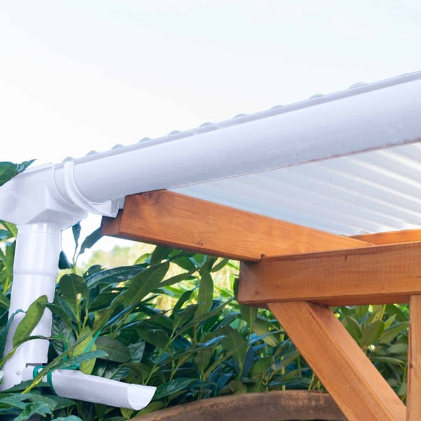 Weiße PVC-Dachrinne mit Fallrohr und Konsolrinnenhaltern an einer Holzkonstruktion