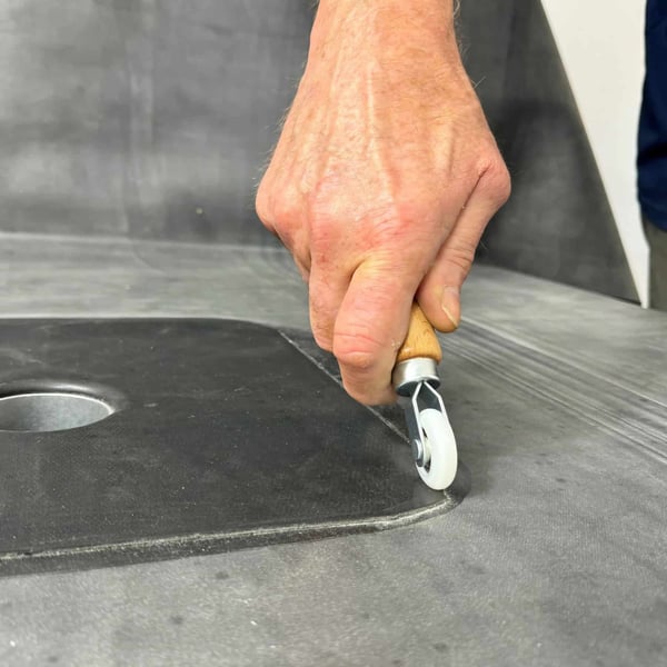 Hand rollt mit Metall-Eckenroller eine dunkle Dachbahn an einer Ecke fest