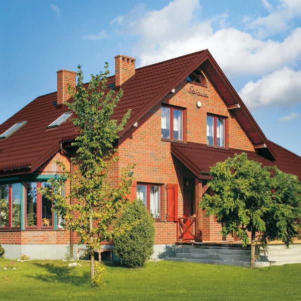Pfannenblech Szafir 350/15 in Rotbraun auf dem Dach eines roten Backsteinhauses mit Gauben