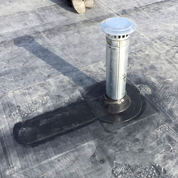 Detailansicht einer schwarzen EPDM Rohrmanschette um ein silbernes Entlueftungsrohr auf einem Flachdach