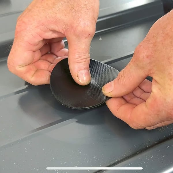 Hände positionieren einen schwarzen EPDM Schrauben Reparaturflicken auf einem Trapezblech