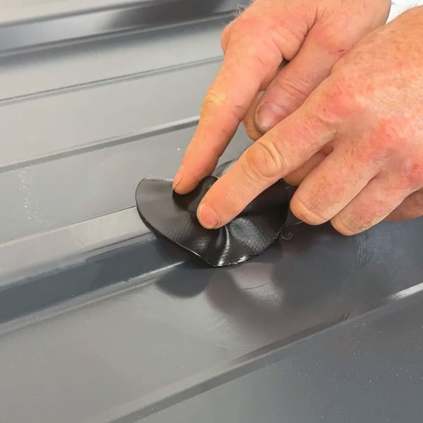 Hände drücken einen schwarzen EPDM Schrauben Reparaturflicken auf ein graues Trapezblech