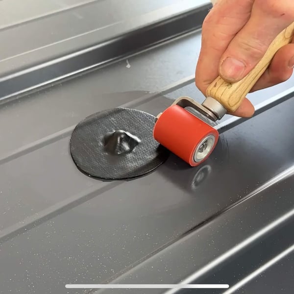 Hand rollt mit Andrückrolle einen schwarzen EPDM Schrauben Reparaturflicken auf Trapezblech