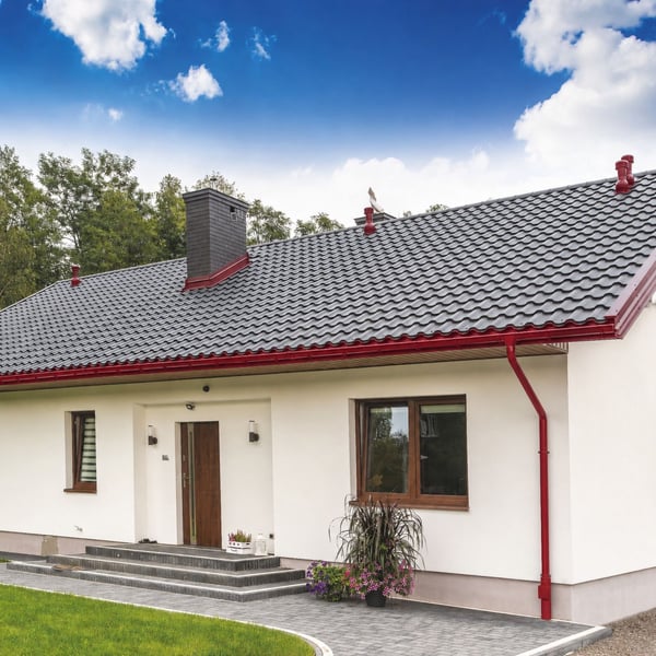 Gesamtansicht eines weissen Hauses mit dunklem Dach und komplett montiertem kirschrotem Niagara Dachrinnensystem