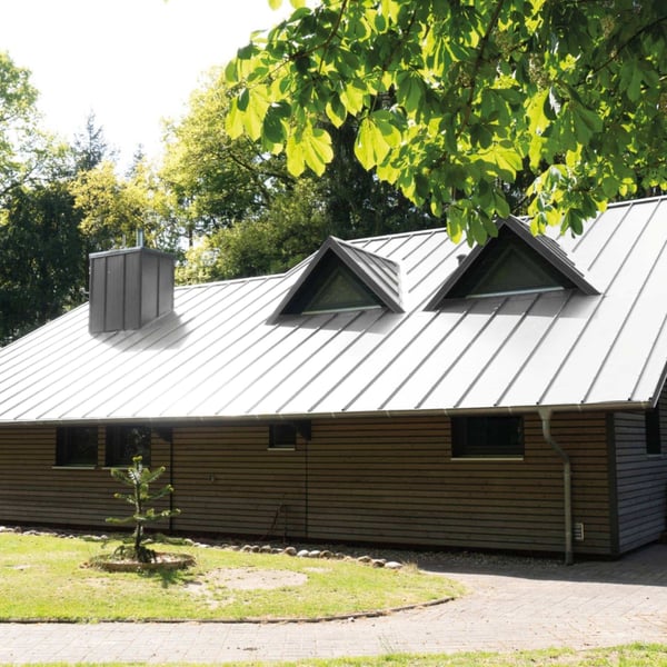 Stehfalzblech in Weißaluminium (RAL 9006) auf einem Wohnhaus mit Gauben und Schornstein