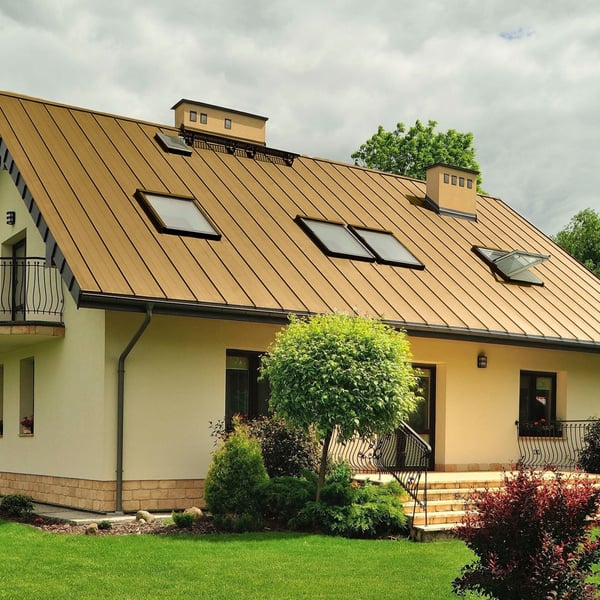 Einfamilienhaus mit sandgelbem Stehfalzblechdach PD-510-S Flach, umgeben von Garten und Baeumen
