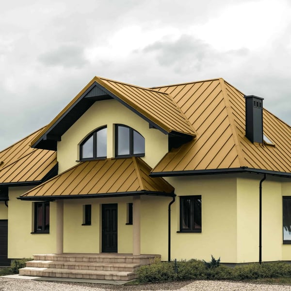 Stehfalzblech PD-510-S Mikro Sandgelb auf einem Wohnhaus mit Gauben und dunklen Dachrinnen