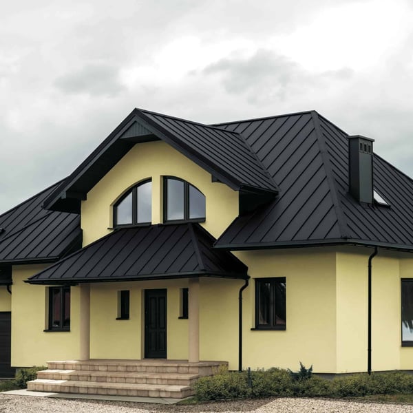 Stehfalzblech PD-510-S Mikro Graphitgrau auf einem Hausdach mit gelber Fassade und Gauben