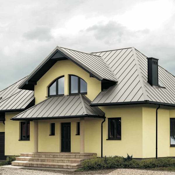Stehfalzblech PD-510-S Mikro, Grauweiß RAL 9002, auf einem Hausdach mit gelber Fassade