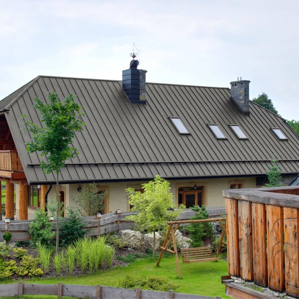 Stehfalzblech PD-510-S Graualuminium auf einem Hausdach mit mehreren Dachfenstern und Schornstein