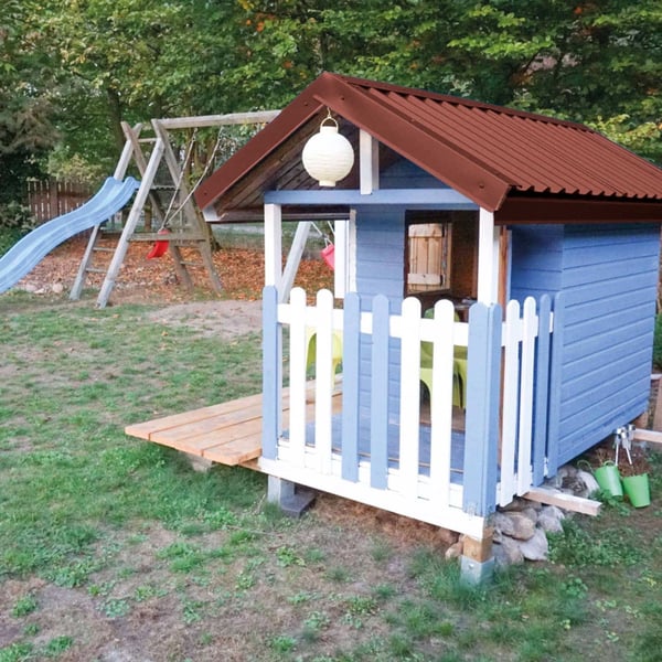 Trapezblech 20/1100 rotbraun auf dem Dach eines blauen Kinderspielhauses mit Rutsche im Hintergrund