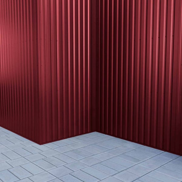 Ecke einer weinroten Trapezblech 20/1100 Wand, vertikal verlegt, mit Pflastersteinen