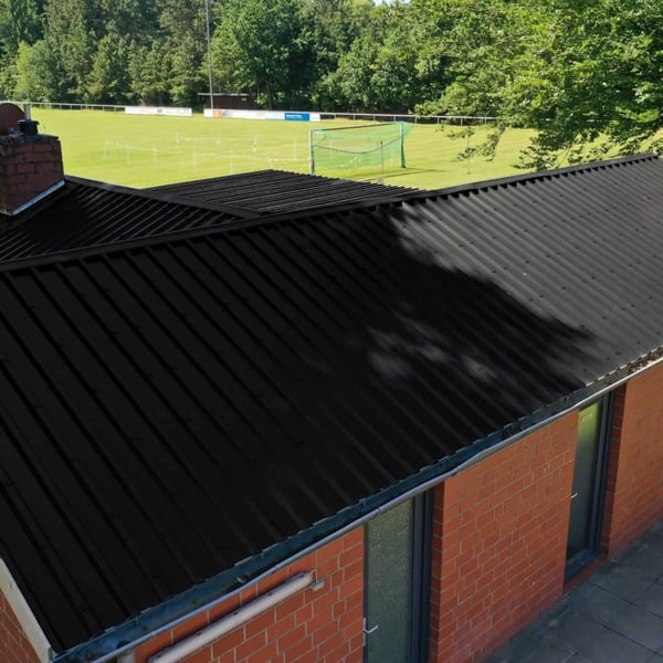Trapezblech 35/207 Tiefschwarz auf dem Dach eines Backsteingebäudes neben einem Sportplatz