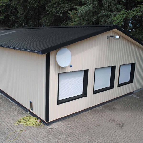Trapezblech 35/207 Anthrazitgrau auf einem hellen Gebäude mit Satellitenschüssel, Verlegung auf einem Dach