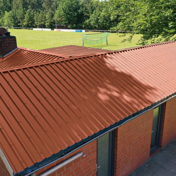 Trapezblech 35/207 in Kupferbraun auf einem Ziegelgebäude mit Blick auf ein Fussballfeld