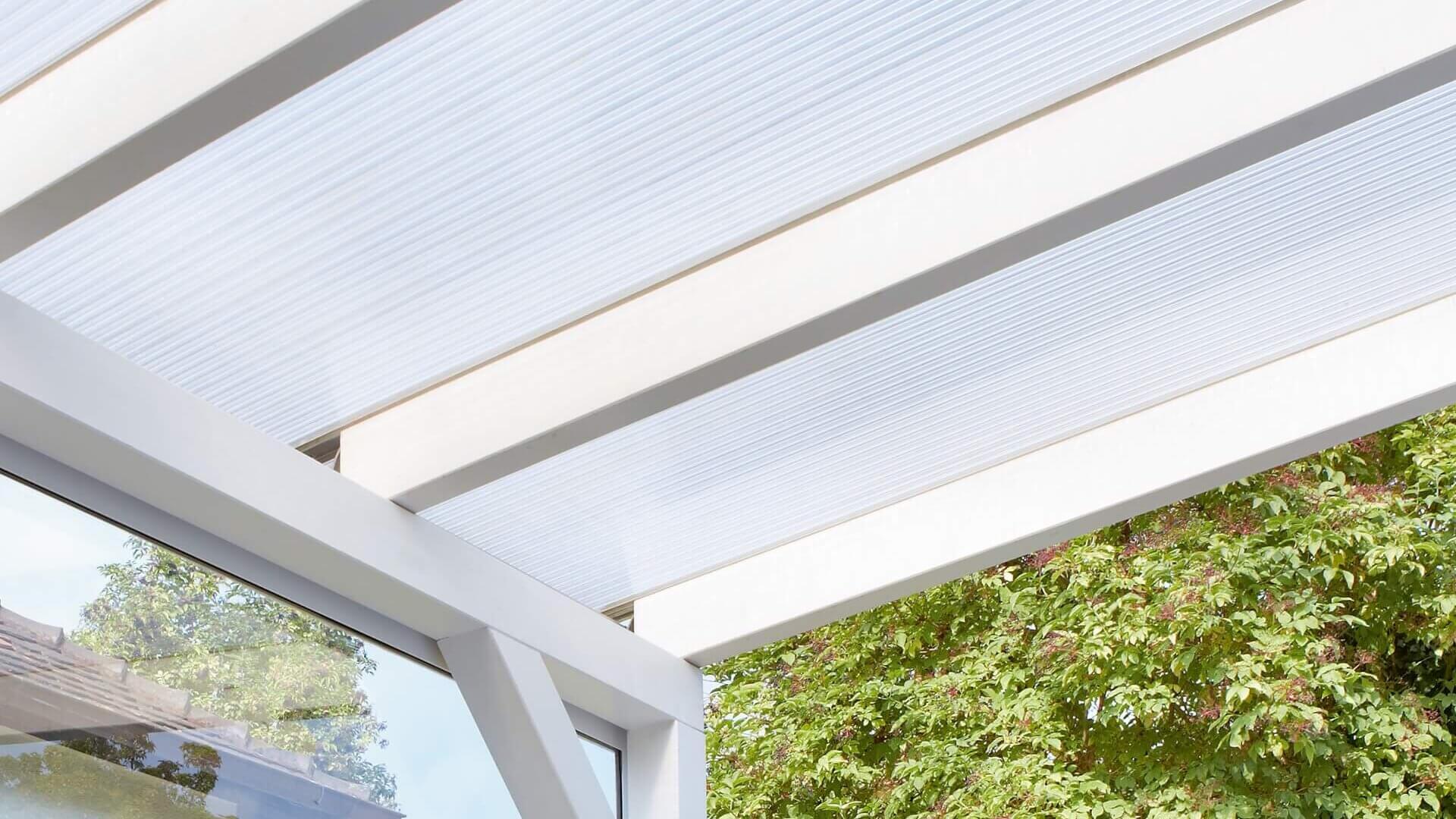 Das Bild zeigt eine Terrassenüberdachung mit Stegplatten.
Die Unterkonstruktion ist weiß., die Stegplatten klar.