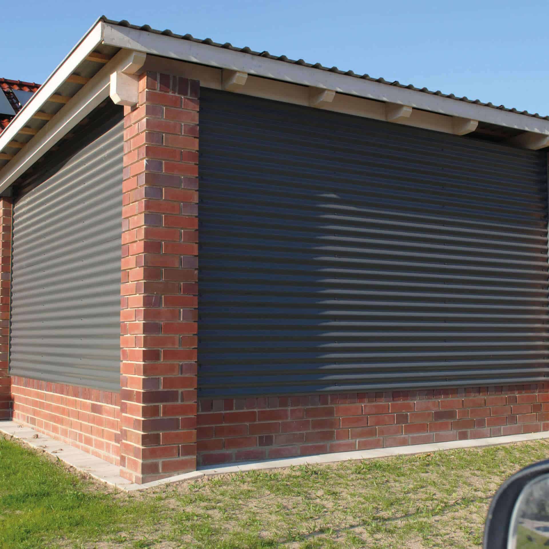 Eine moderne Garage mit Wellblechverkleidung und stabilen Ziegelpfeilern. Die dunklen Wellblechpaneele sorgen für eine robuste und stilvolle Optik.