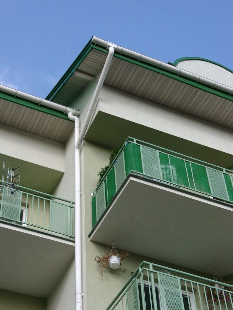 Mehrparteienhaus mit grünen Akzenten und einer weißen Kunststoffdachrinne.