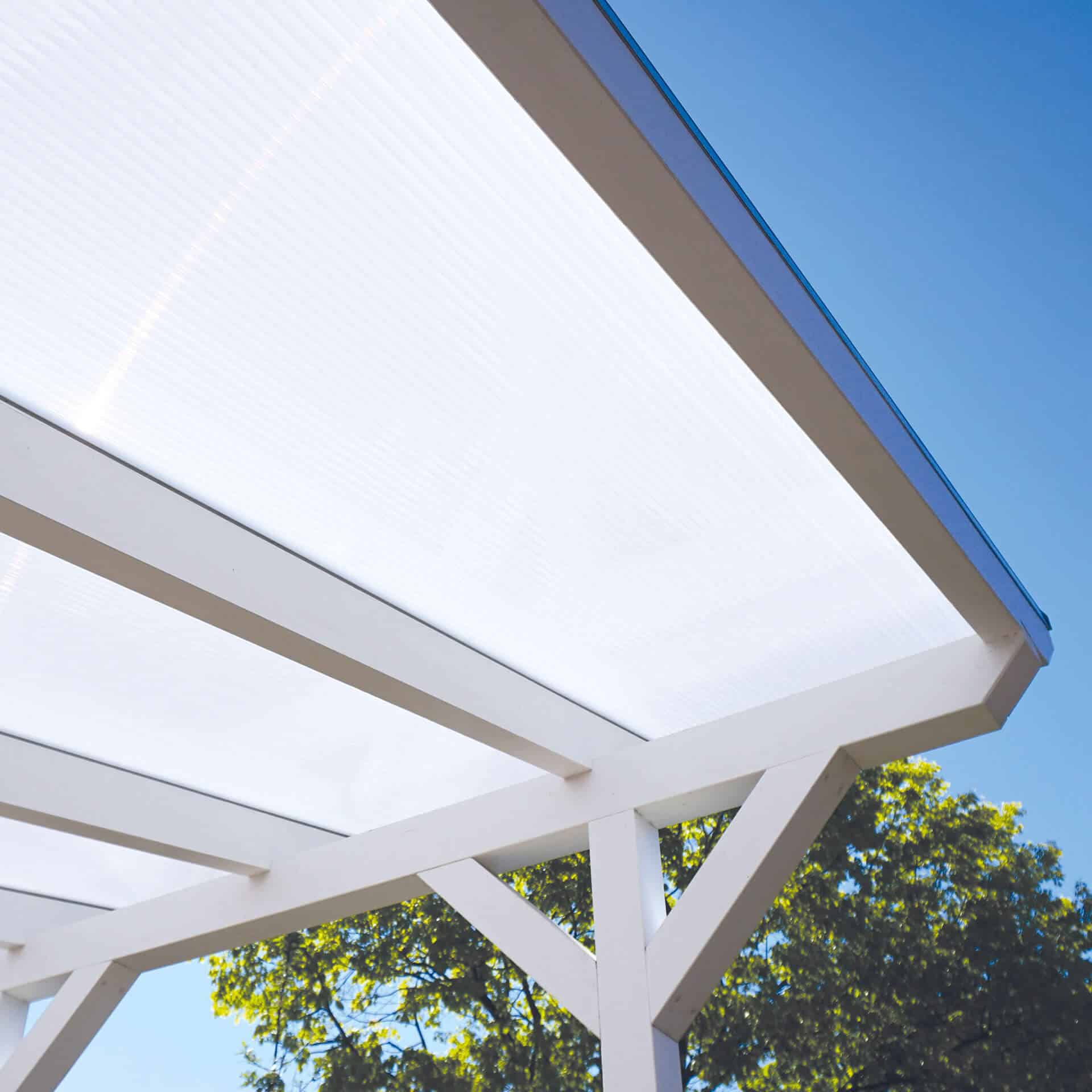 Detailansicht einer weißen Terrassenüberdachung mit lichtdurchlässiger Stegplatte als Dacheindeckung, aufgenommen aus der Froschperspektive bei klarem Himmel und Baumkrone im Hintergrund.