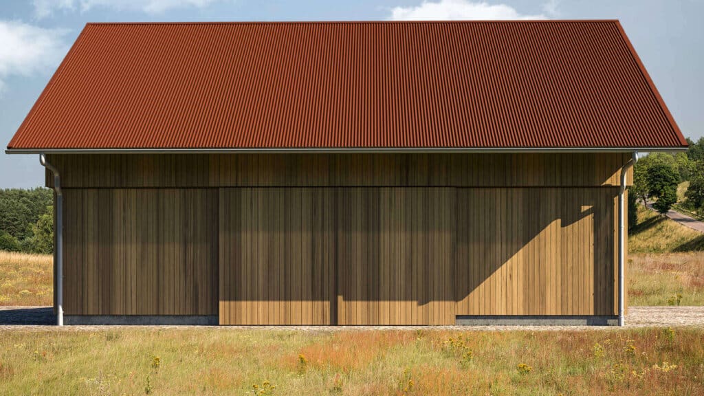 Scheunenartiges Gebäude mit Fassade aus senkrecht verlegten Holzprofilen und rotbraunem Dach aus eng gewellten Profilplatten, gelegen in einer offenen Wiesenlandschaft unter blauem Himmel.
