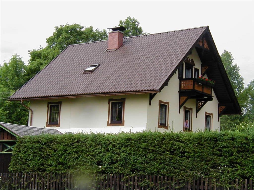 Wohnhaus mit creme farbenen Putz und braunen Akzenten, dazu die Dacheindeckung aus farblich passenden brauen Pfannenblechen