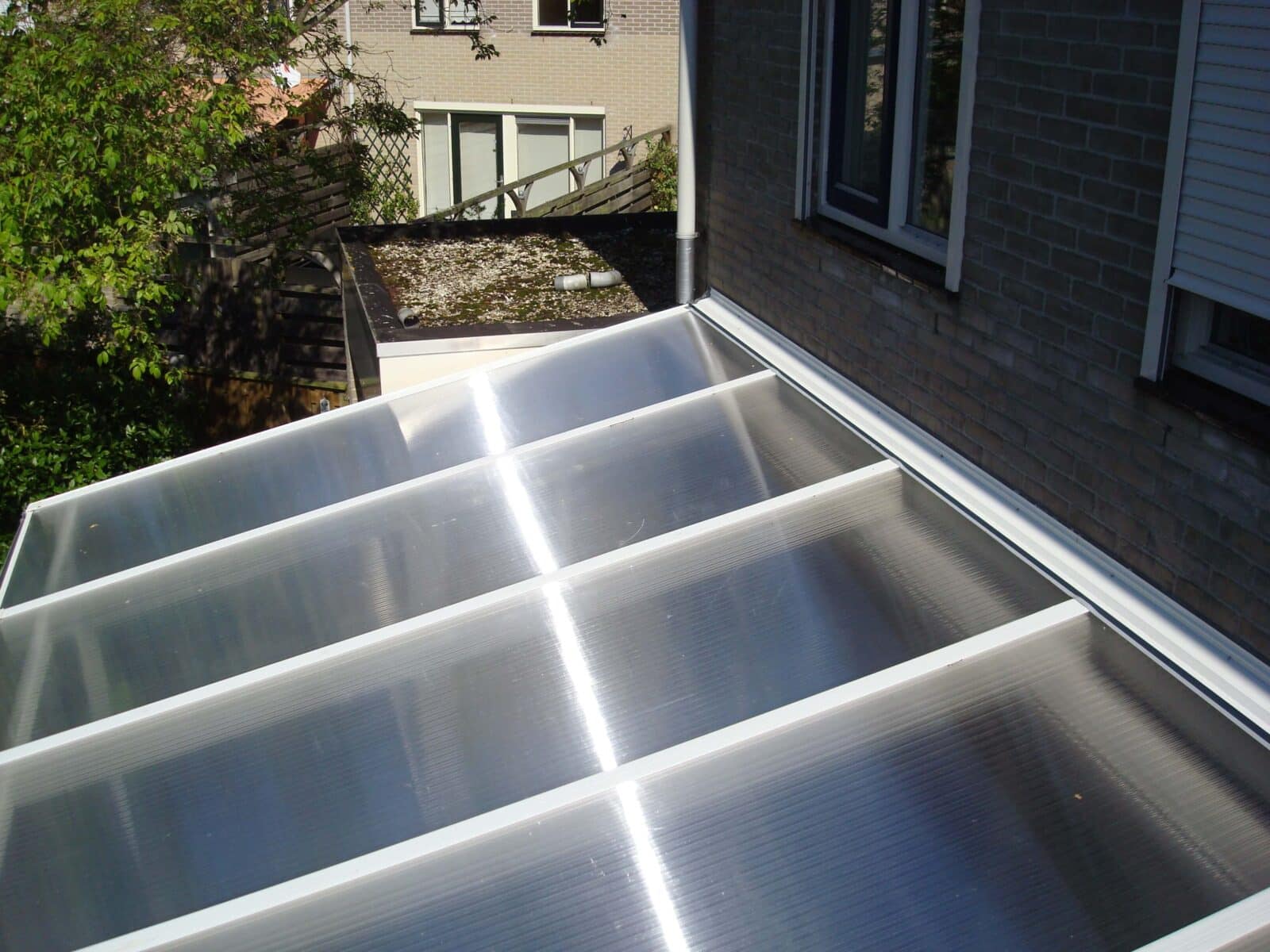 Ansicht von oben auf eine Überdachung aus klaren Stegplatten mit weißen Montageprofilen, sichtbarer Reflexionsstreifen durch die Sonne.