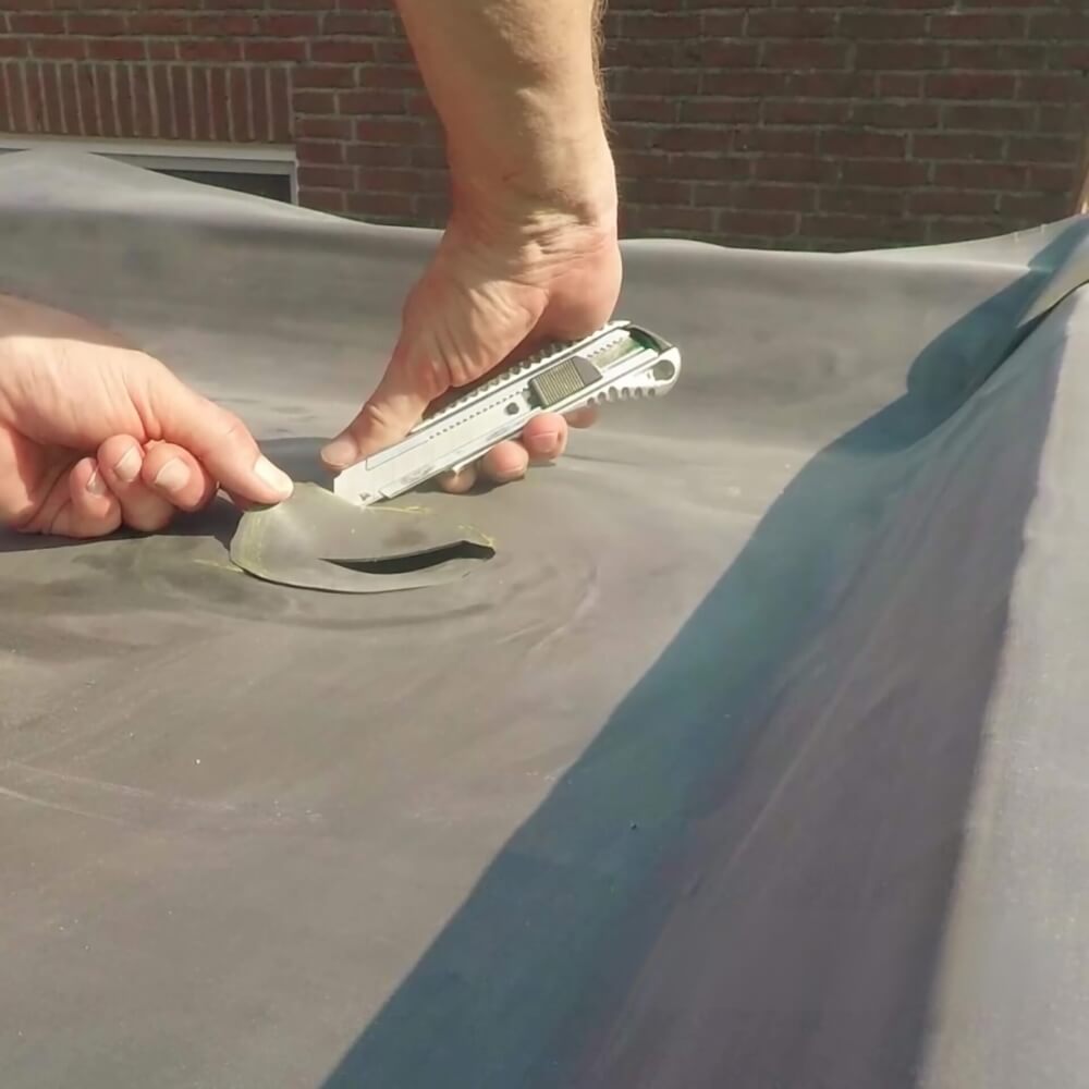 Eine Person führt eine Reparatur an einer EPDM-Dachfolie durch, indem sie mit einem Cutter ein Stück beschädigter Folie ausschneidet