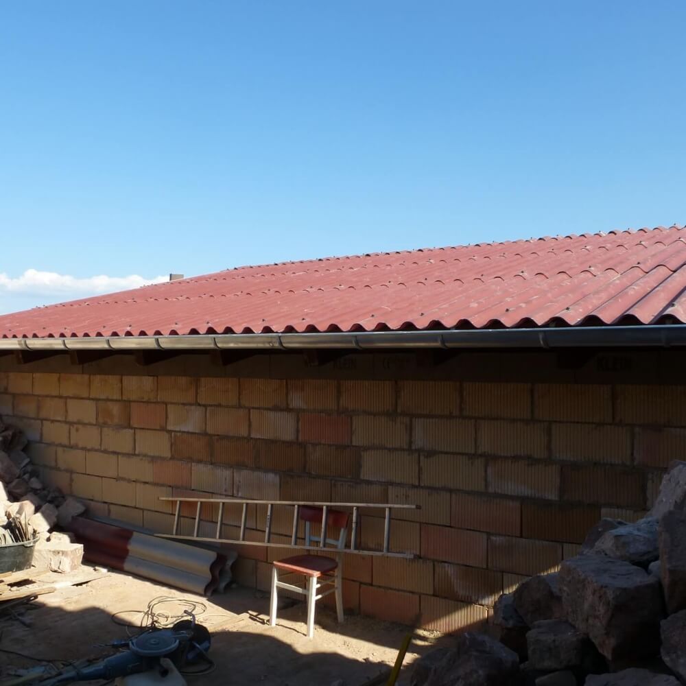 Neu verlegtes Dach mit roten Faserzement Wellplatten, Baustelle im Vordergrund