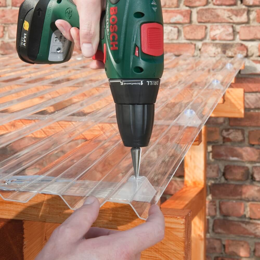Handwerkliche Montage von durchsichtigen Wellplatten mit einem Akkubohrschrauber auf einem Holzdachstuhl, präzise und effiziente Heimwerkerarbeit